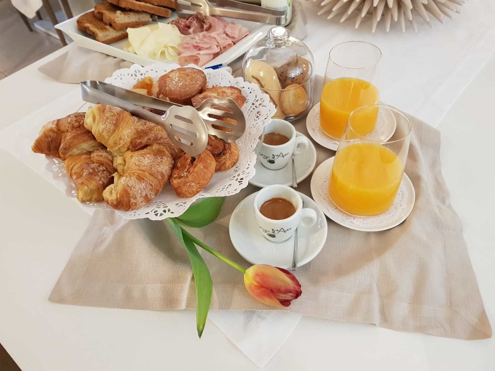 Ein Frühstücksbrett mit Croissants, Käse, Schinken und Brot, dazu Kaffee und Orangensaft.
