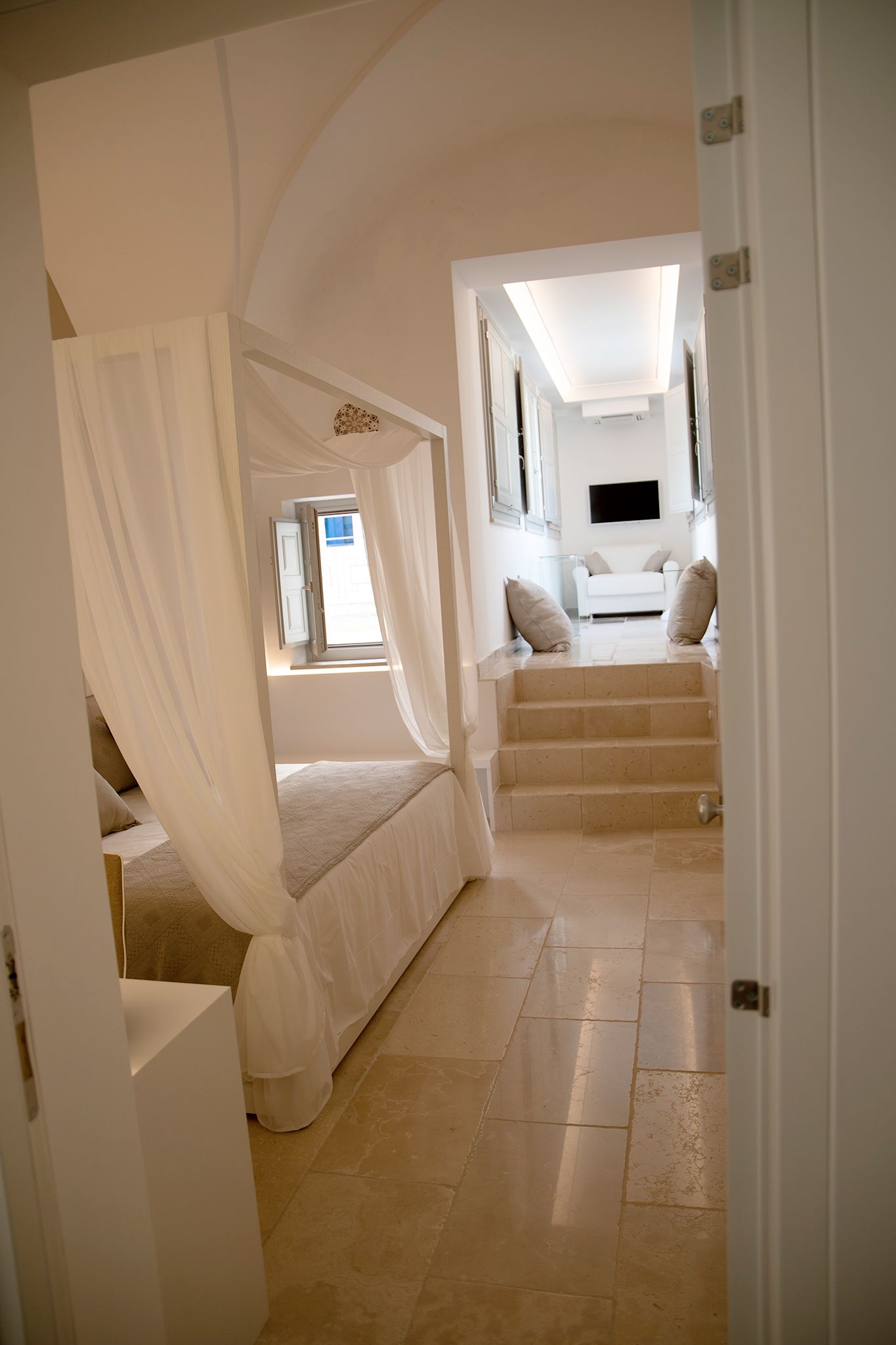 Un dormitorio con cama con dosel, una escalera que conduce a una sala de estar con sofá y televisor.