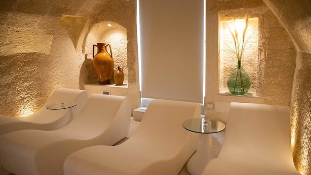 A spa room with two white cushioned chairs, a small table, and a vase with reeds. - Monun Hotel & Spa  (Grottaglie)