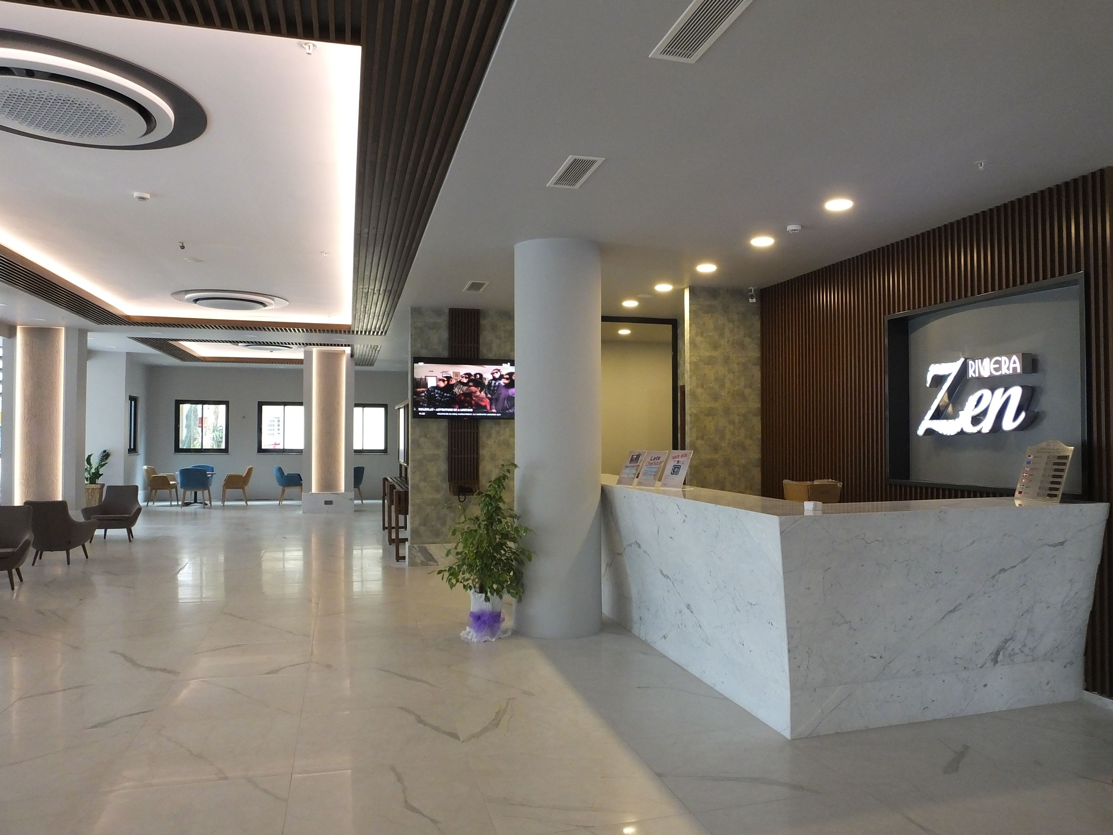 A hotel reception area with a marble counter, a television mounted on the wall, and a sign reading "Riviera Zen".