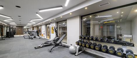 A modern gym with exercise equipment, weight racks, and a large mirror.