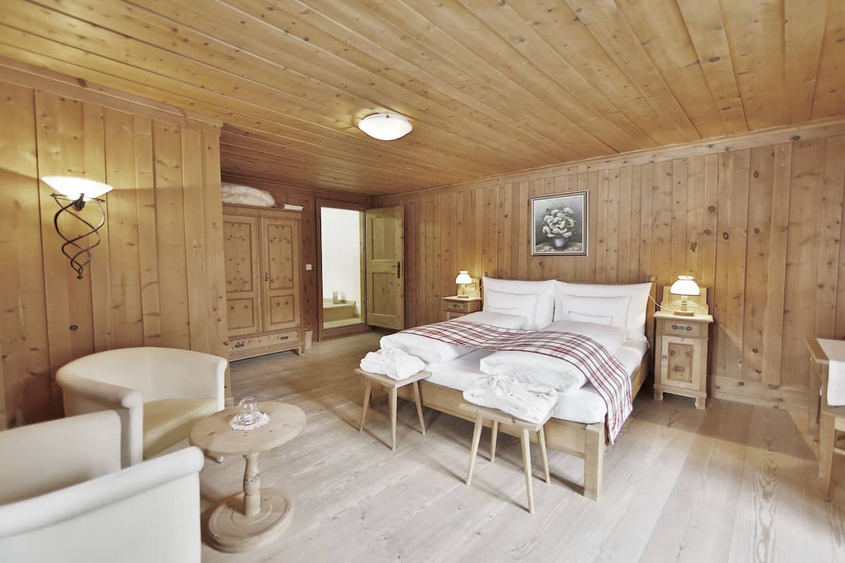 Une pièce aux murs lambrissés, comprenant un lit, deux tables de chevet avec des lampes, une chaise, une petite table ronde et un miroir.