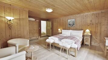 A wooden-paneled room with a bed, two bedside tables with lamps, a chair, a small round table, and a mirror.
