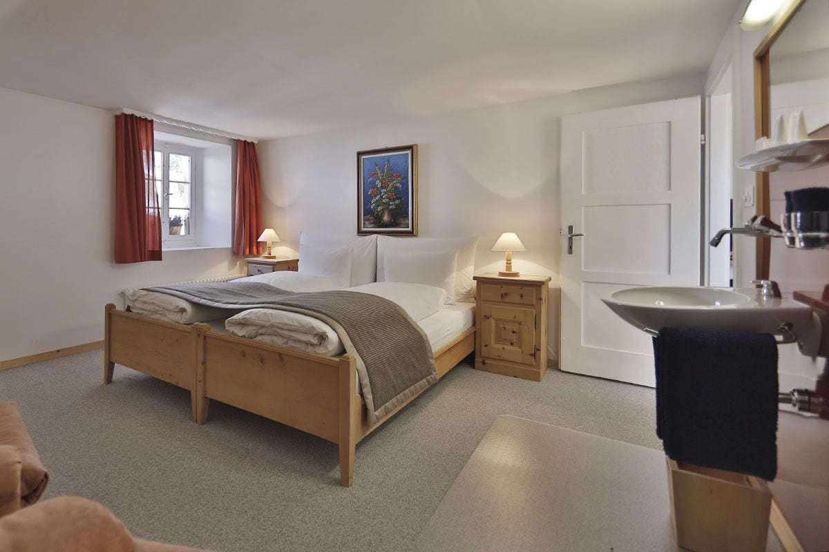 A bedroom with a wooden bed, bedside tables with lamps, a white door, and a bathroom with a sink and mirror.