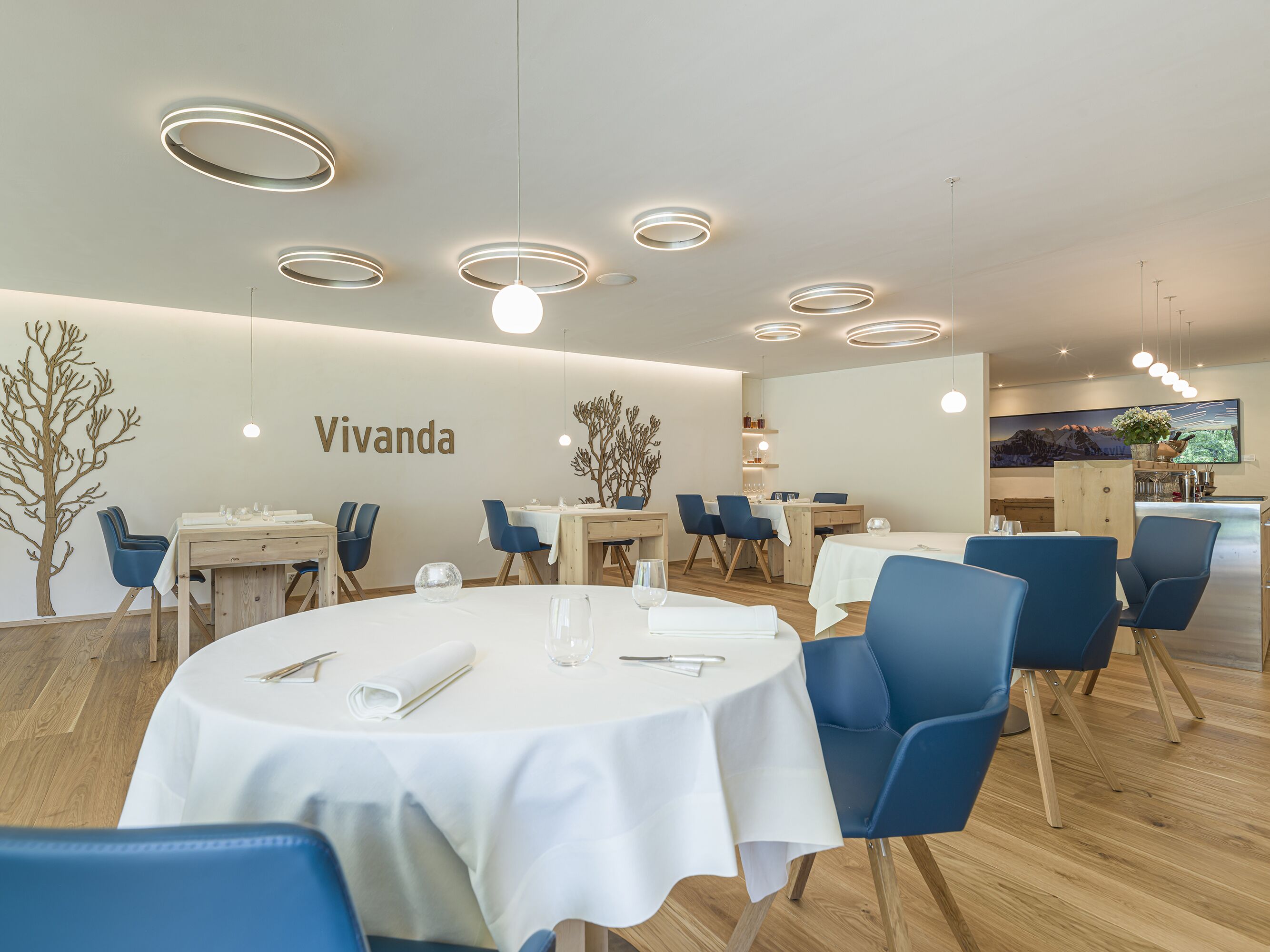 A modern dining area with round tables, blue chairs, and a 'Vivanda' sign on the wall.