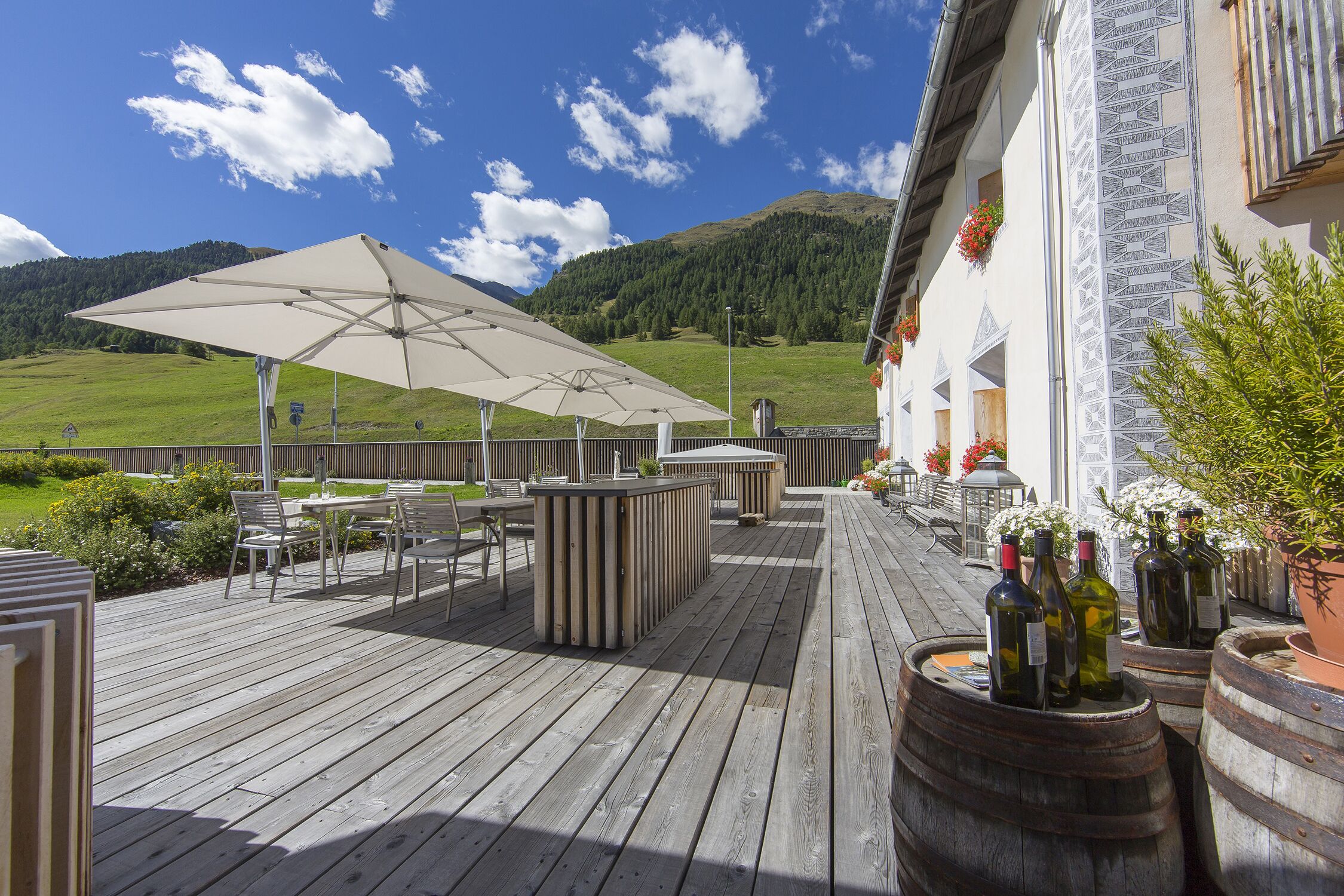 Una terraza de madera con asientos exteriores, zona de bar y botellas de vino.