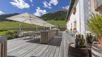 Una terraza de madera con asientos exteriores, zona de bar y botellas de vino.