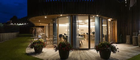 A modern building with a curved wooden exterior, a glass entrance, and a well-lit interior.