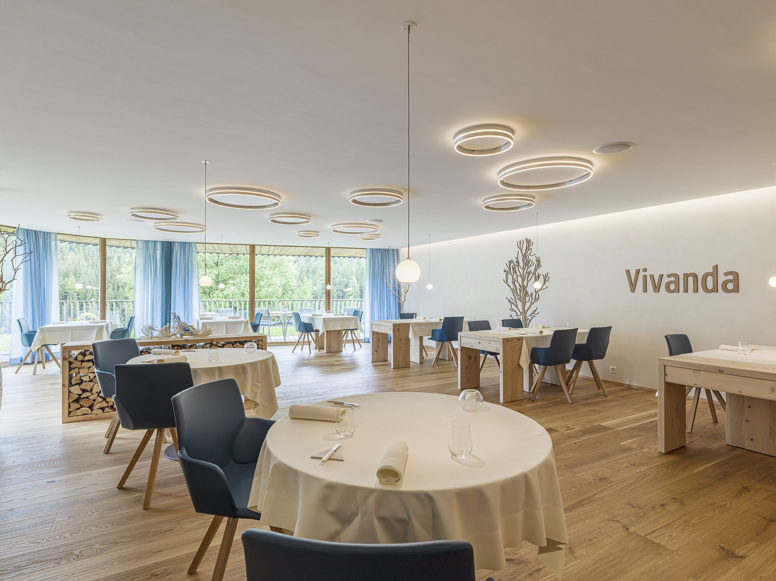 A modern dining area with round tables, blue chairs, and a 'Vivanda' sign on the wall.