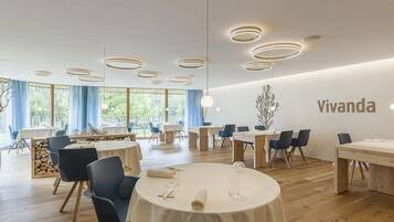 A modern dining area with round tables, blue chairs, and a 'Vivanda' sign on the wall.