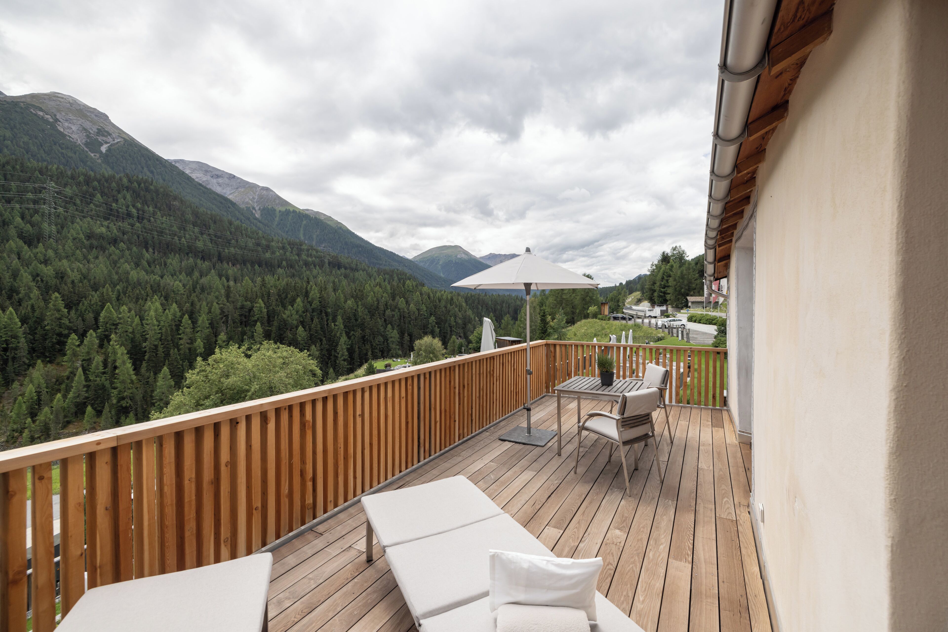 A wooden deck with lounge chairs and a table, overlooking a forested valley and mountains.