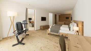 Una habitación de hotel moderna con suelo de madera, cama con ropa blanca, un escritorio con computadora, una silla y una lámpara.