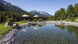 Un lac de montagne aux eaux limpides, bordé d’une rive rocheuse et entouré d’une végétation luxuriante, avec quelques chaises longues placées sous des parasols.