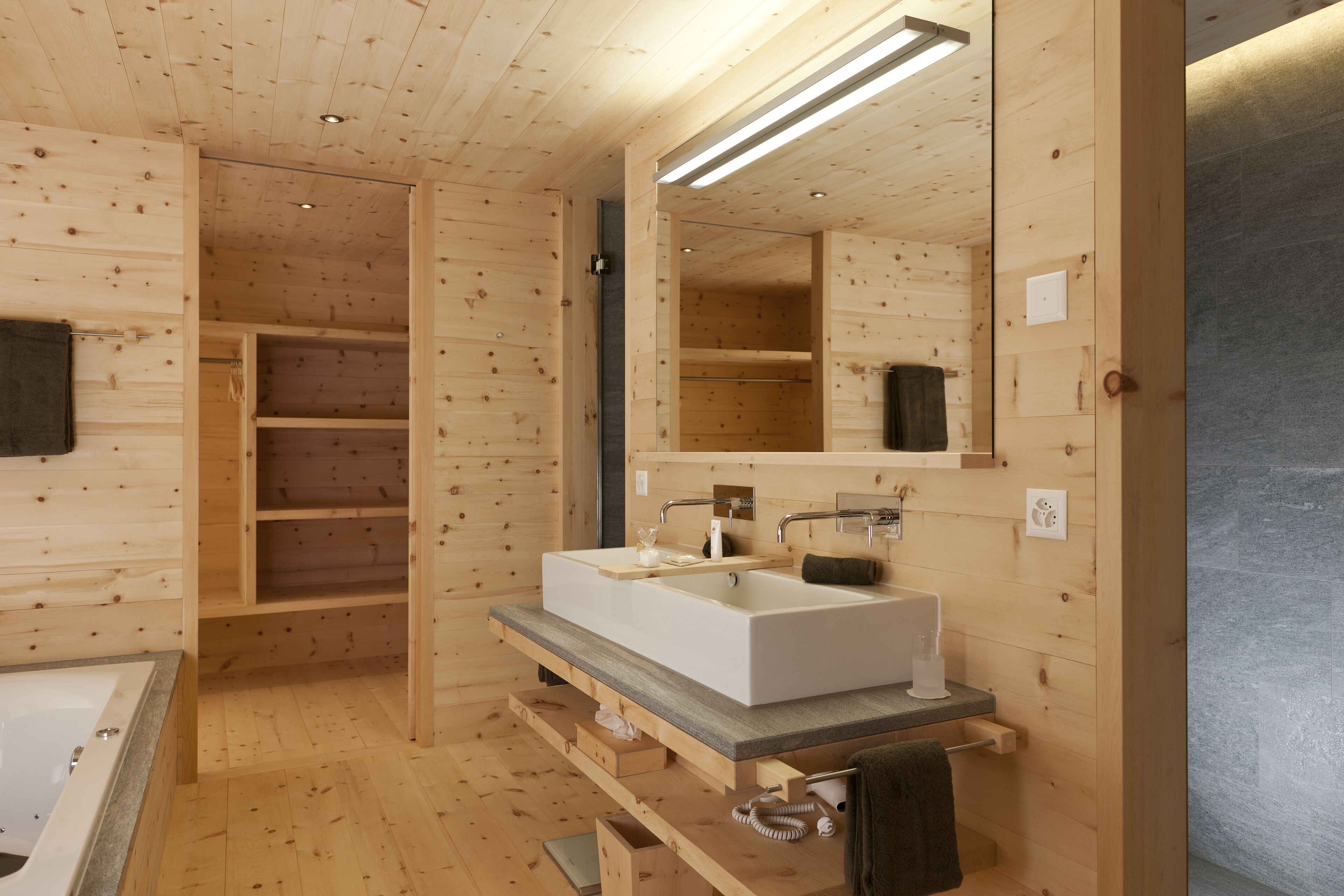 Ein Badezimmer einer Holzhütte mit integriertem Waschbecken, Spiegel und Regalen.