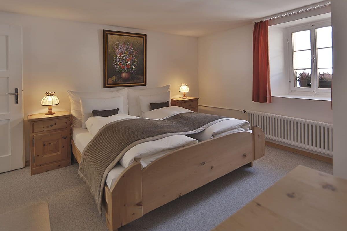 Une chambre à coucher avec un lit en bois, des tables de chevet avec des lampes, un radiateur, une fenêtre avec des rideaux et une porte.