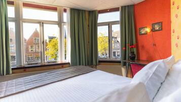 Habitación de hotel con cama, ventana con cortinas, radiador y vista a edificios.