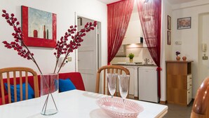Un comedor con una mesa blanca, dos sillas, una cesta rosa y un florero de vidrio con ramas.