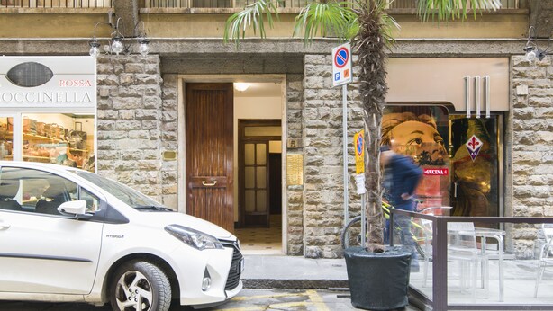 Un coche blanco estacionado frente a un edificio de fachada de piedra y un cartel para Rossa Occinella.