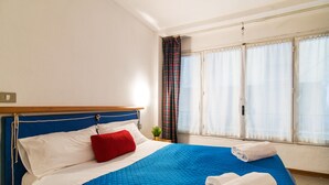 Una cama bien hecha con ropa de cama azul y blanca, una almohada roja y toallas blancas en el suelo.