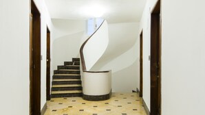 Un pasillo con una escalera de caracol, suelo de mármol y puertas de madera.