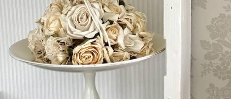 Un pedestal blanco con un arreglo floral y una cesta azul con panes planos.