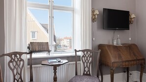 Una habitación con un ventanal grande, un televisor montado en la pared, una mesita con libros y un control remoto, y dos sillas.
