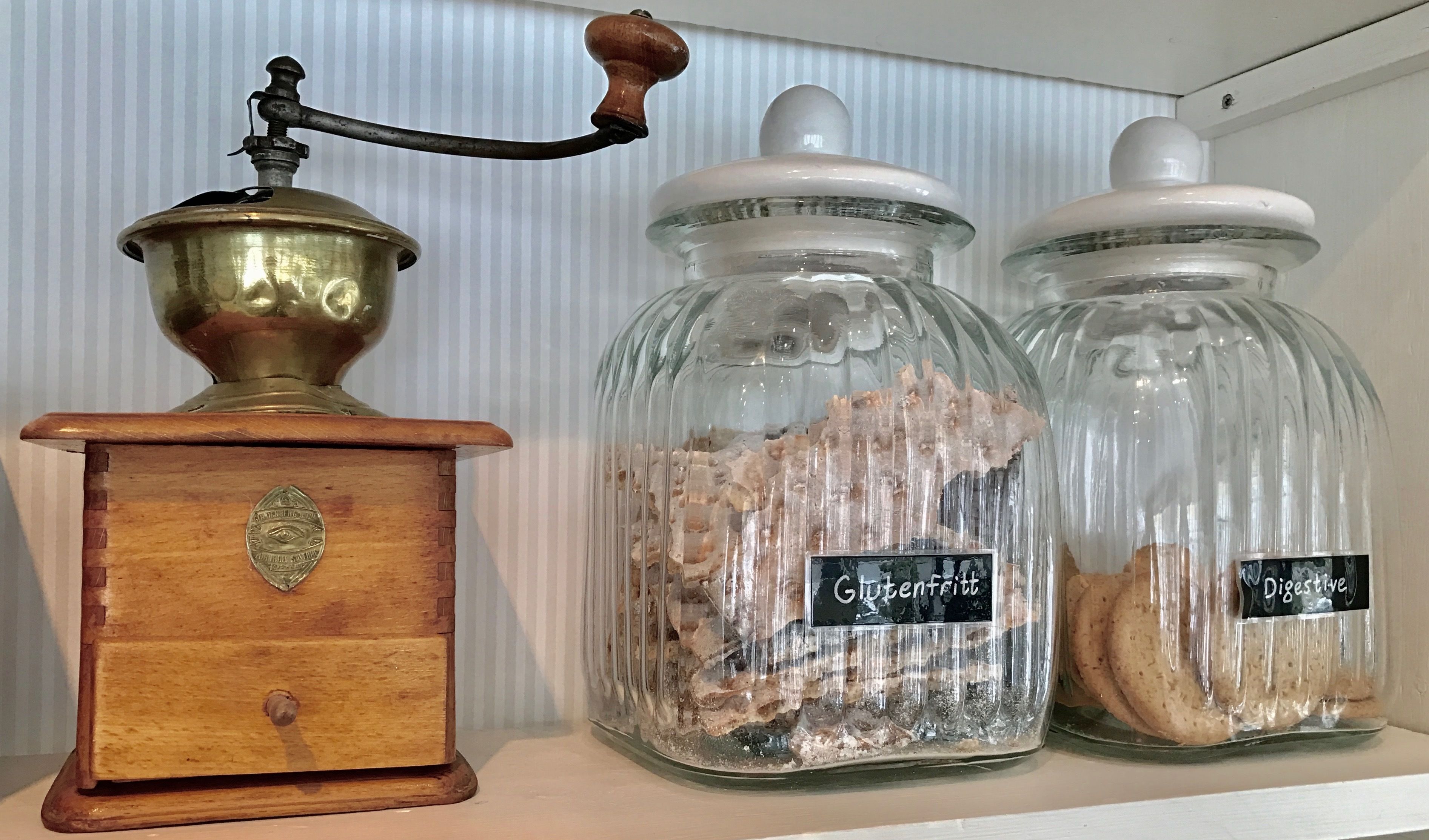 A wooden grain press, two glass jars with labels, and a white shelf.