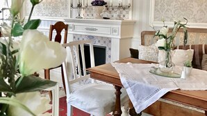 Un comedor con una mesa de madera, sillas blancas, una chimenea y un estante decorativo con platos.