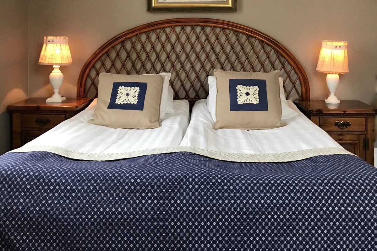Cama bem arrumada com colcha estampada, dois travesseiros com rendas delicadas e uma obra de arte emoldurada sobre a cabeceira.