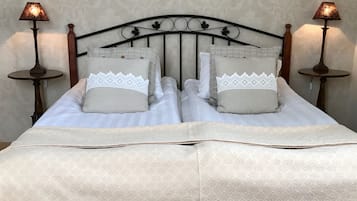 Un lit bien fait, recouvert d’une couvre-lit à motifs, avec deux oreillers ornés de dentelle et deux lampes de chevet sur des supports assortis.