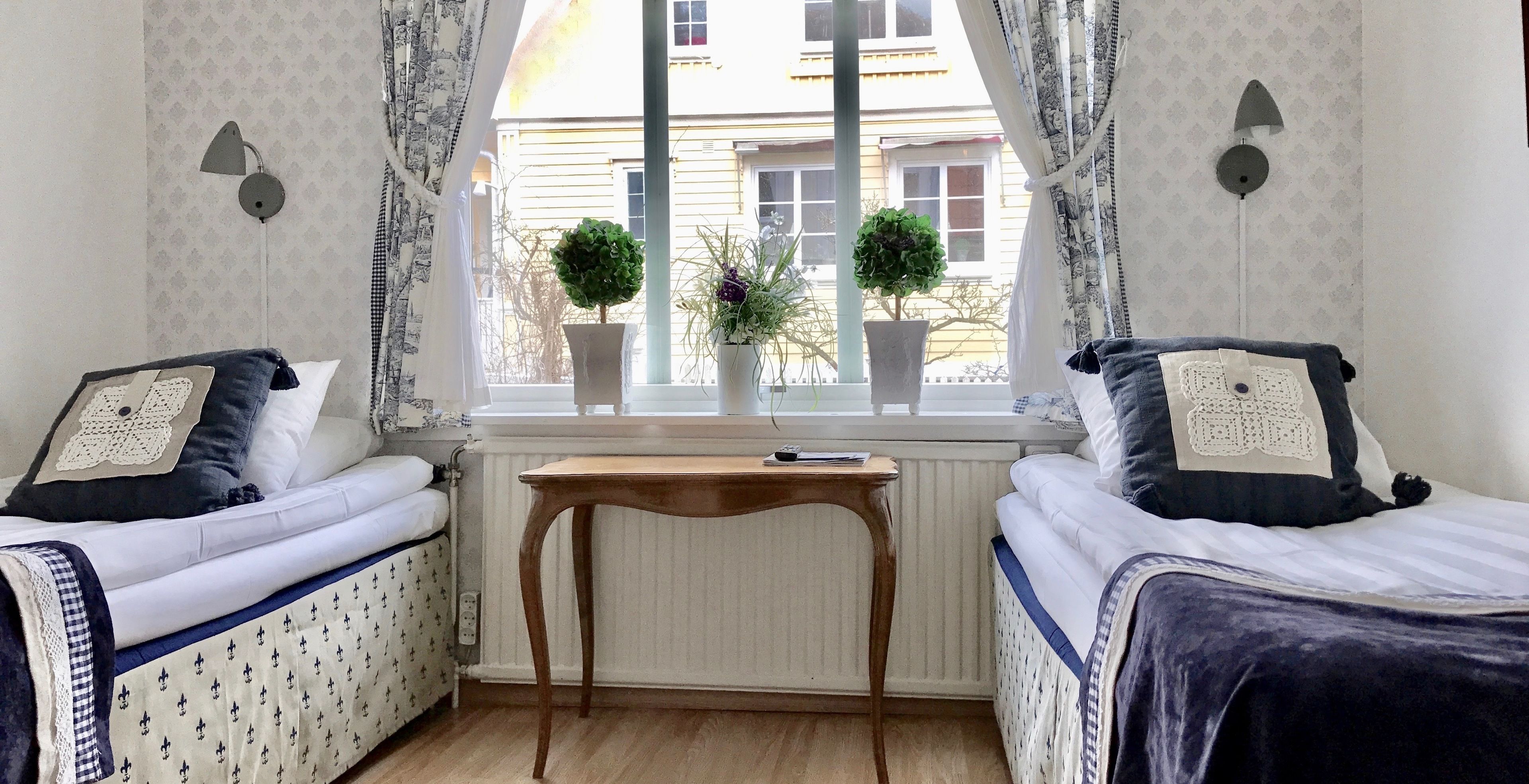Quarto com duas camas, uma mesa e uma janela com plantas em vasos.