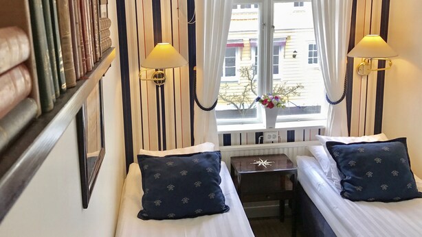 Habitación de hotel con dos camas, una mesita y una ventana con cortinas.