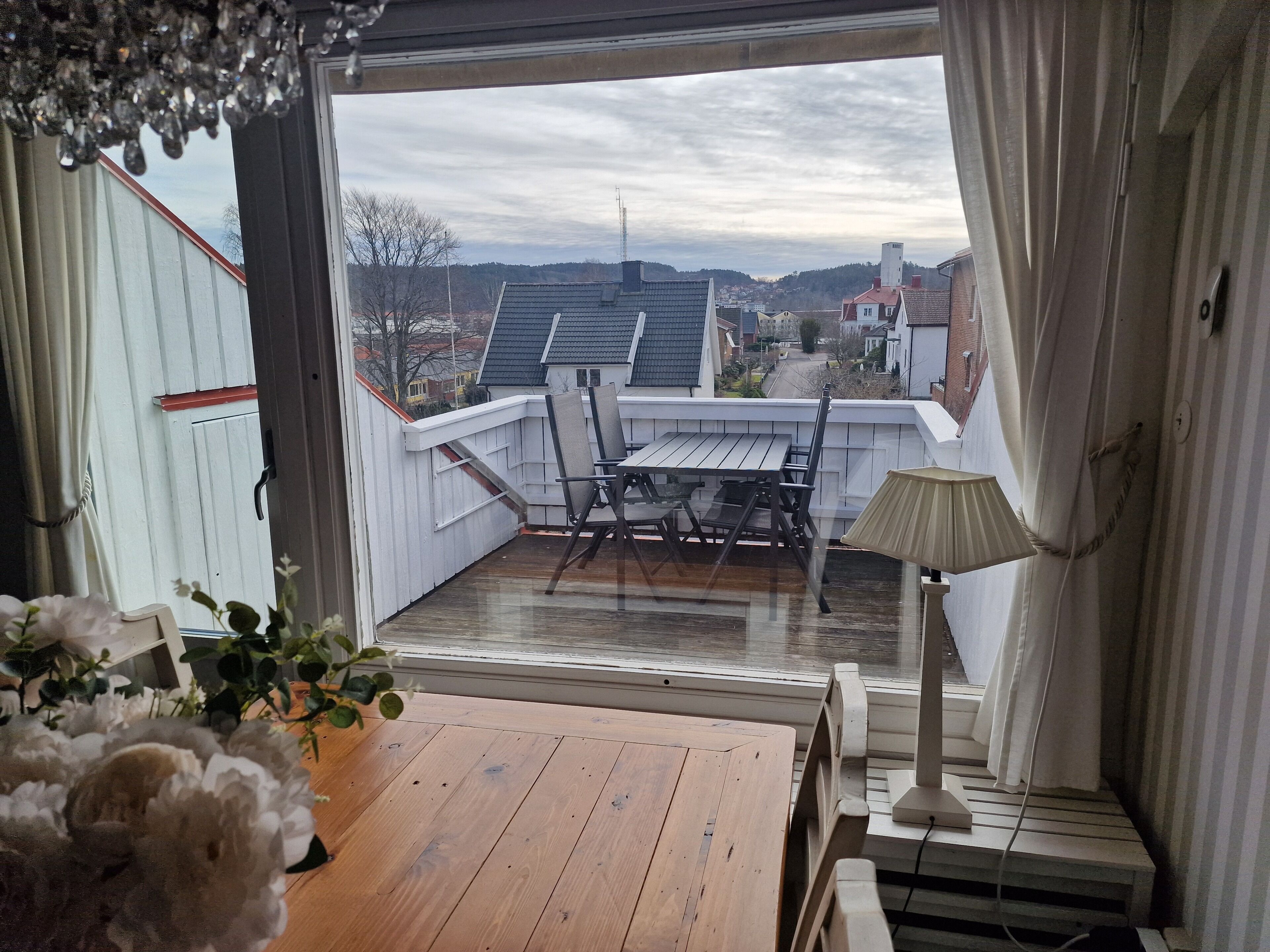 A balcony with a wooden table and chairs, a lamp, and a view of a residential area.