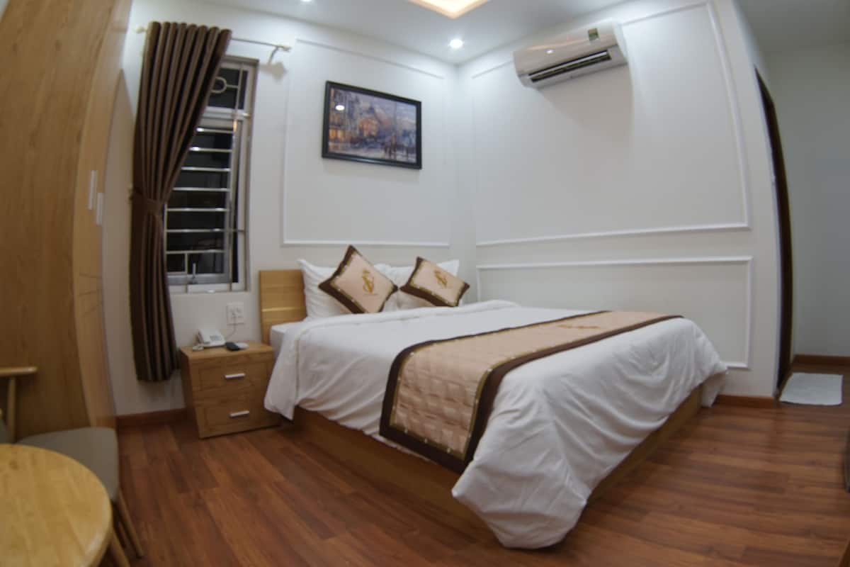 Une chambre d’hôtel comprenant un lit, un bureau, une chaise, une fenêtre avec des rideaux, un appareil de climatisation et un tableau au mur.