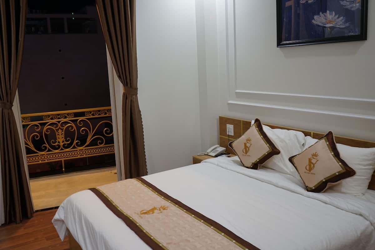 Une chambre d’hôtel avec un lit, des rideaux, une table de chevet, un téléphone et un tableau au mur.