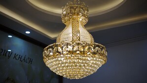 A chandelier with a gold and crystal design, hanging from a ceiling with a circular pattern. - Khach San Sao Viet (Quy Nhon)