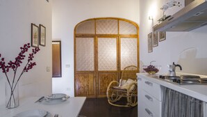 A modern kitchen with white cabinetry, a dining table set with plates and cutlery, a wicker chair, and a decorative vase with red berries.