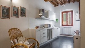 A kitchen with white cabinets, a stainless steel range hood, and a wicker chair.