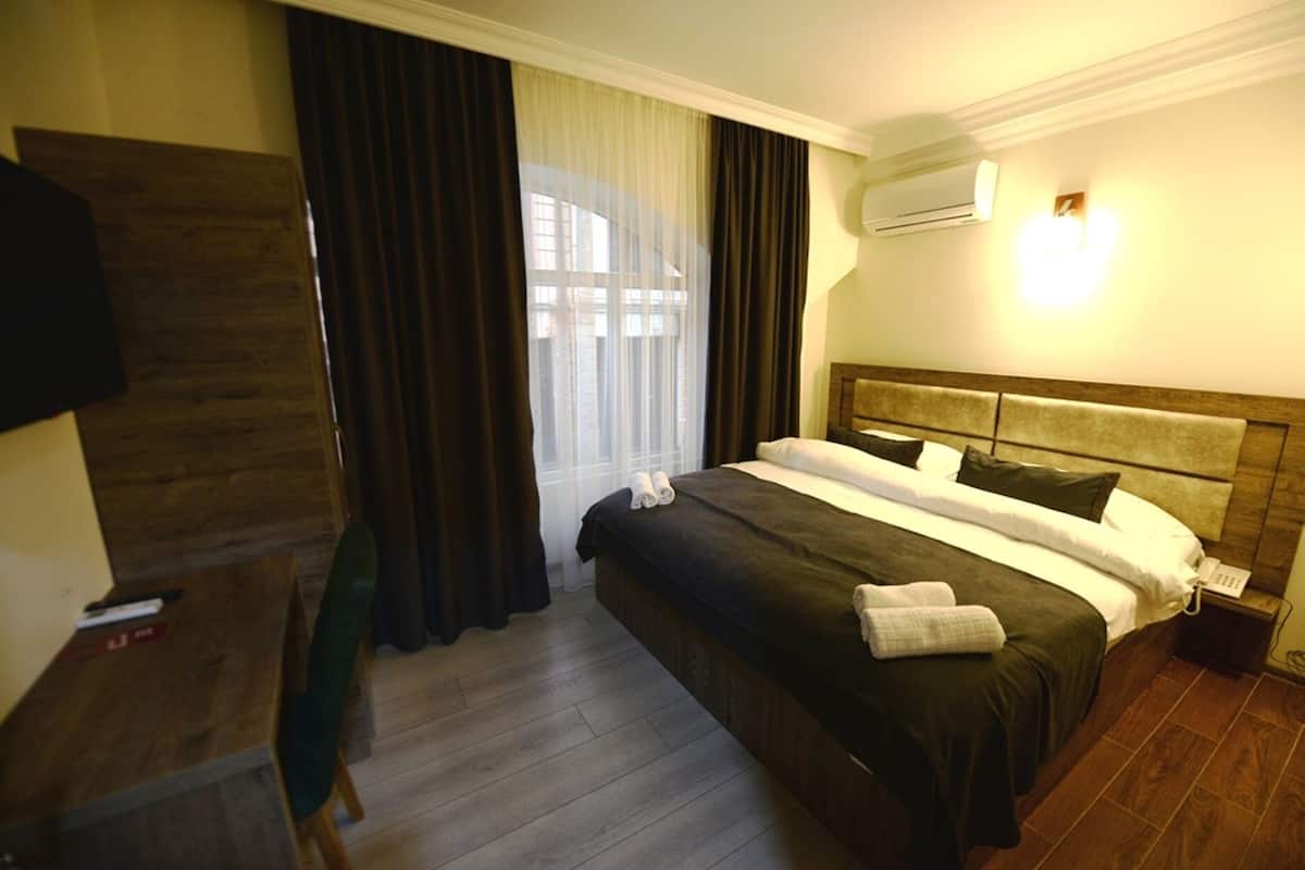 Hotellihuone, jossa on sänky, työpöytä, tuoli, televisio ja ilmastointilaite.