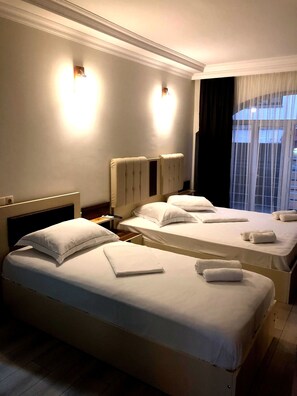 Habitación de hotel con dos camas, cada una con sábanas y toallas blancas impecables. Hay lámparas de pared a ambos lados de las camas.