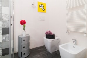 Ein Badezimmer mit einem weißen Waschbecken, einer Toilette, einem Waschtisch mit Schubladen, einer Duschkabine aus Glas und einem Handtuchhalter an der Wand.