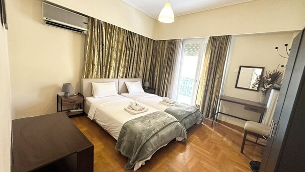 A bedroom with two beds, a bedside table, a lamp, a chair, and a desk. - Comfortable apartment for your holidays, in the center of Athens. (Kallithea)