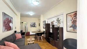A modern living room with a grey sofa, a dining table, and a TV stand. - Comfortable apartment for your holidays, in the center of Athens. (Kallithea)