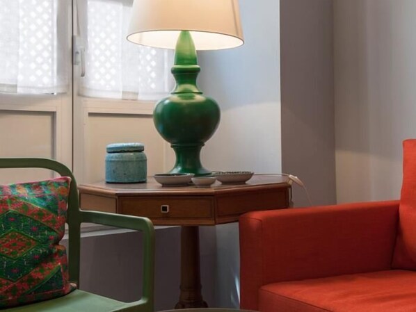 A room with a green chair, a red sofa, a small wooden table with a lamp, and a window with curtains.
