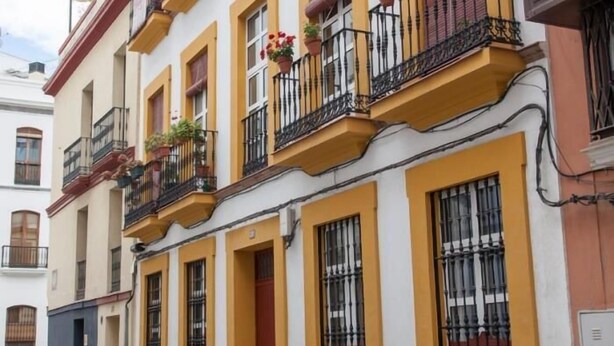 A row of traditional European-style buildings with yellow and white facades, multiple balconies with black railings, and windows with metal bars. - BEAUTIFUL APT DESIGN 1 BED SEVILLA CENTRO-FULL_AC (Sevilla)