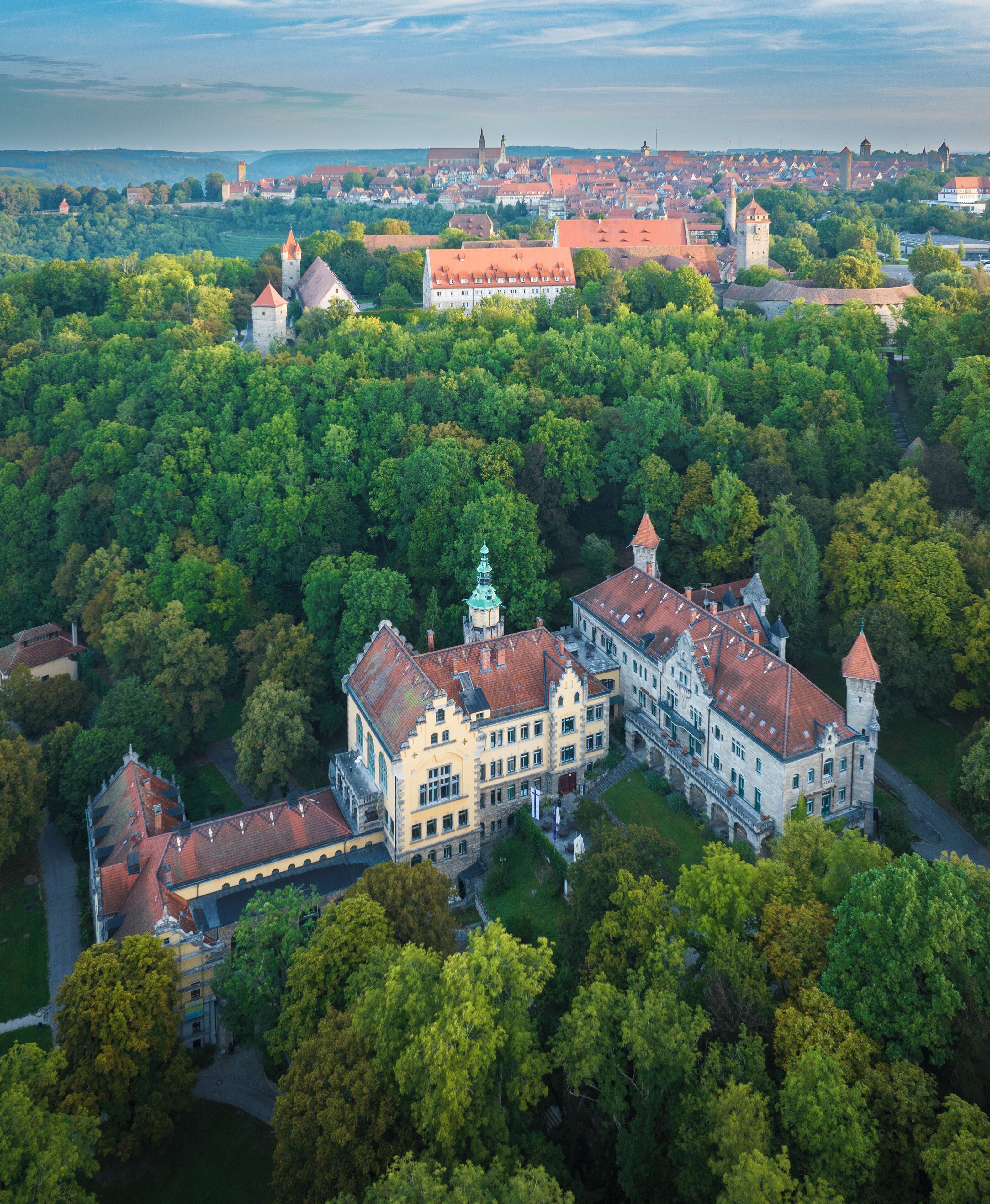 An aerial view of a historic building surrounded by dense greenery, featuring a prominent tower and a large courtyard.