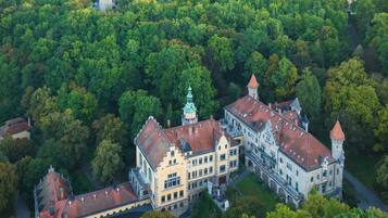 An aerial view of a historic building surrounded by dense greenery, featuring a prominent tower and a large courtyard.