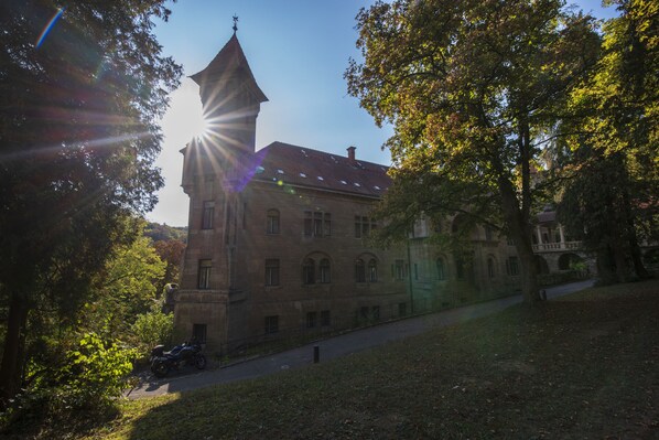 A historic building with a prominent tower and arched windows, surrounded by trees and a clear sky.