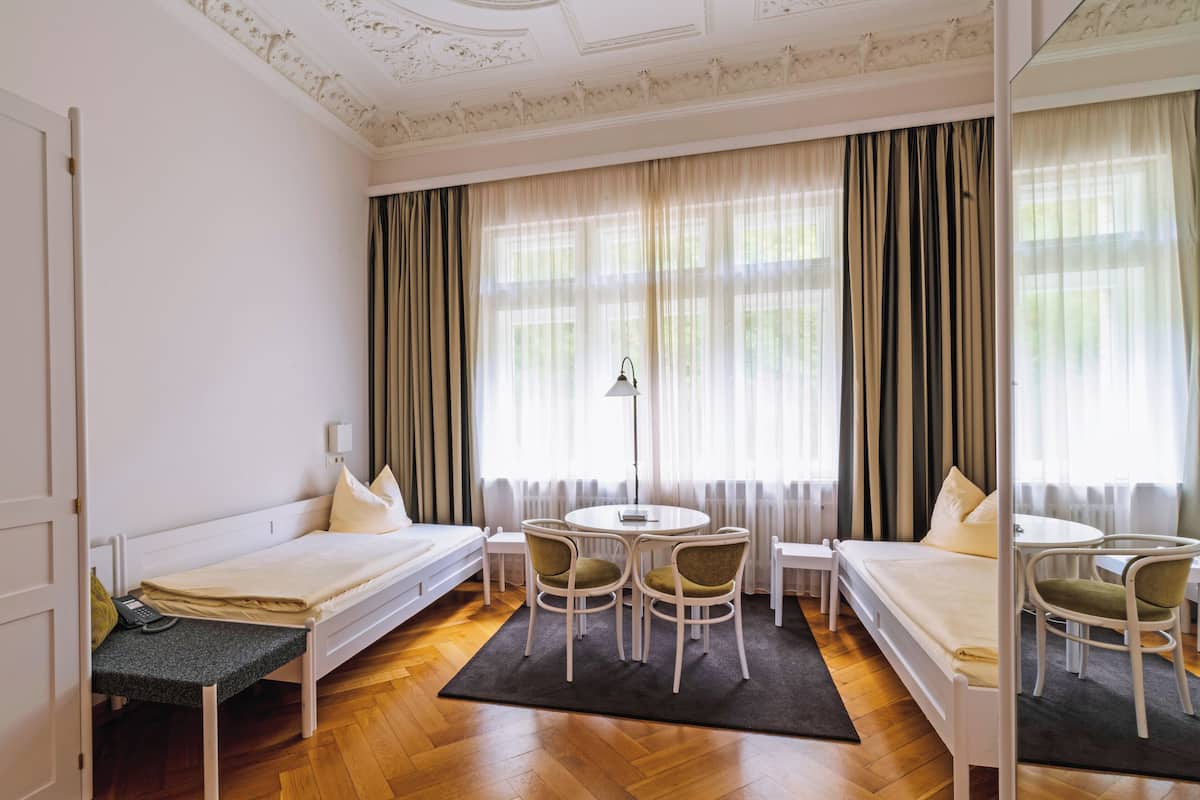 A hotel room with a bed, two chairs, a small table, and a lamp.