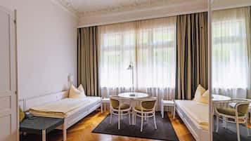 A hotel room with a bed, two chairs, a small table, and a lamp.